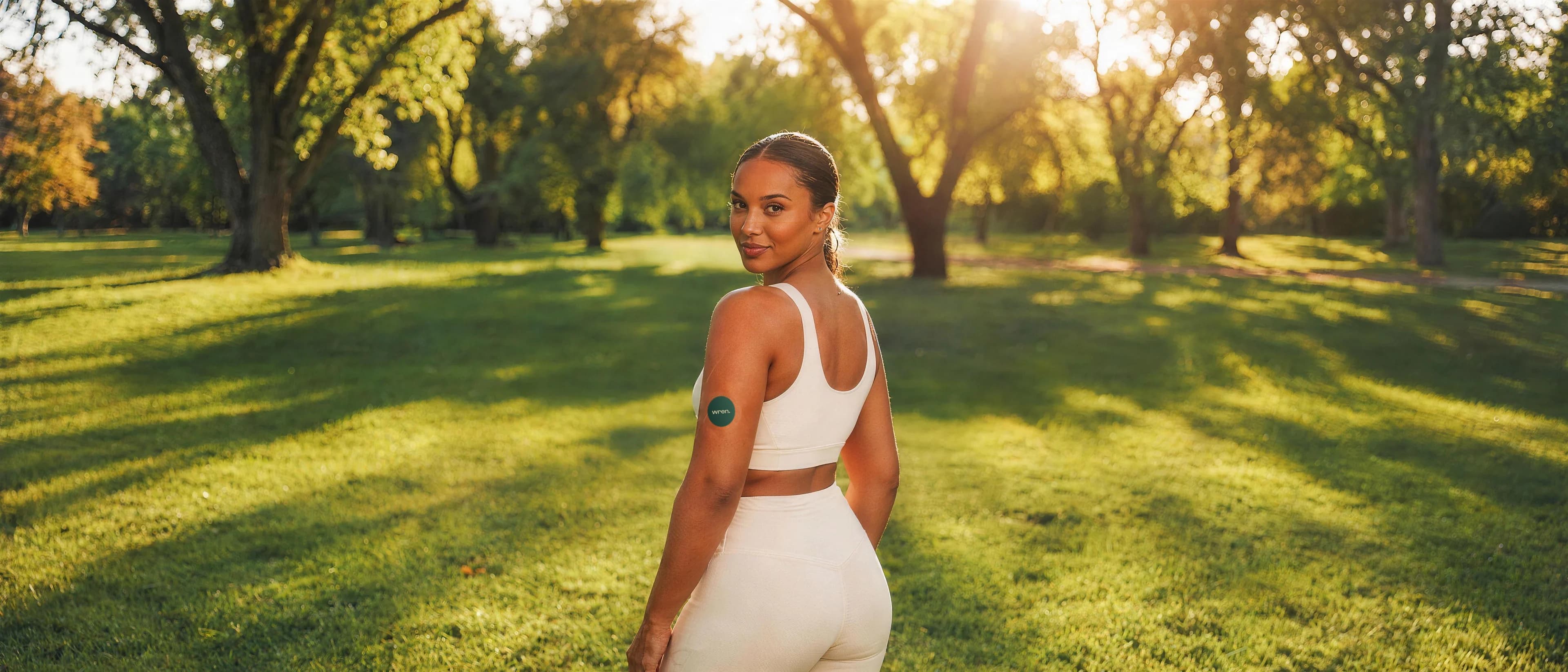 Woman in a sunlit park wearing a Wren glucose sensor on the back of her upper arm